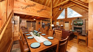 Eine Holzhütte mit Essbereich, Wohnzimmer, Kamin und großen Fenstern.