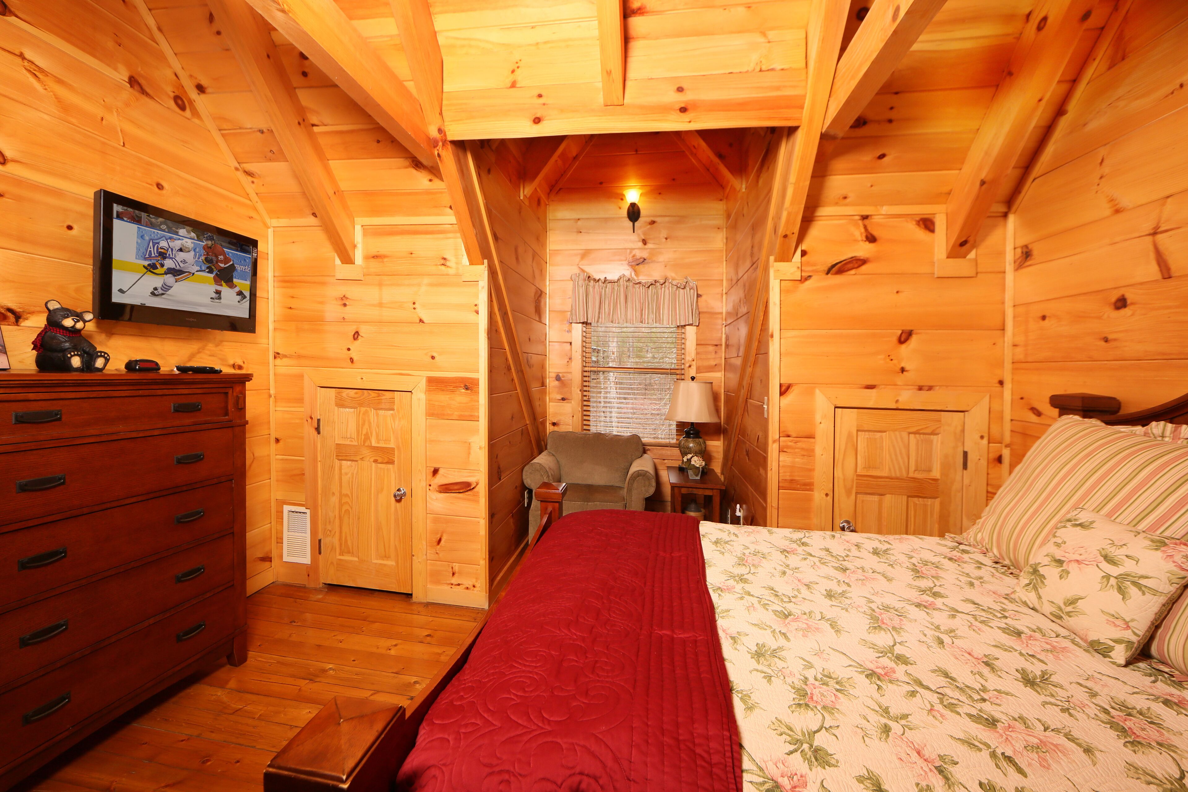 A wooden cabin room with a bed, dresser, and a television displaying a hockey game.