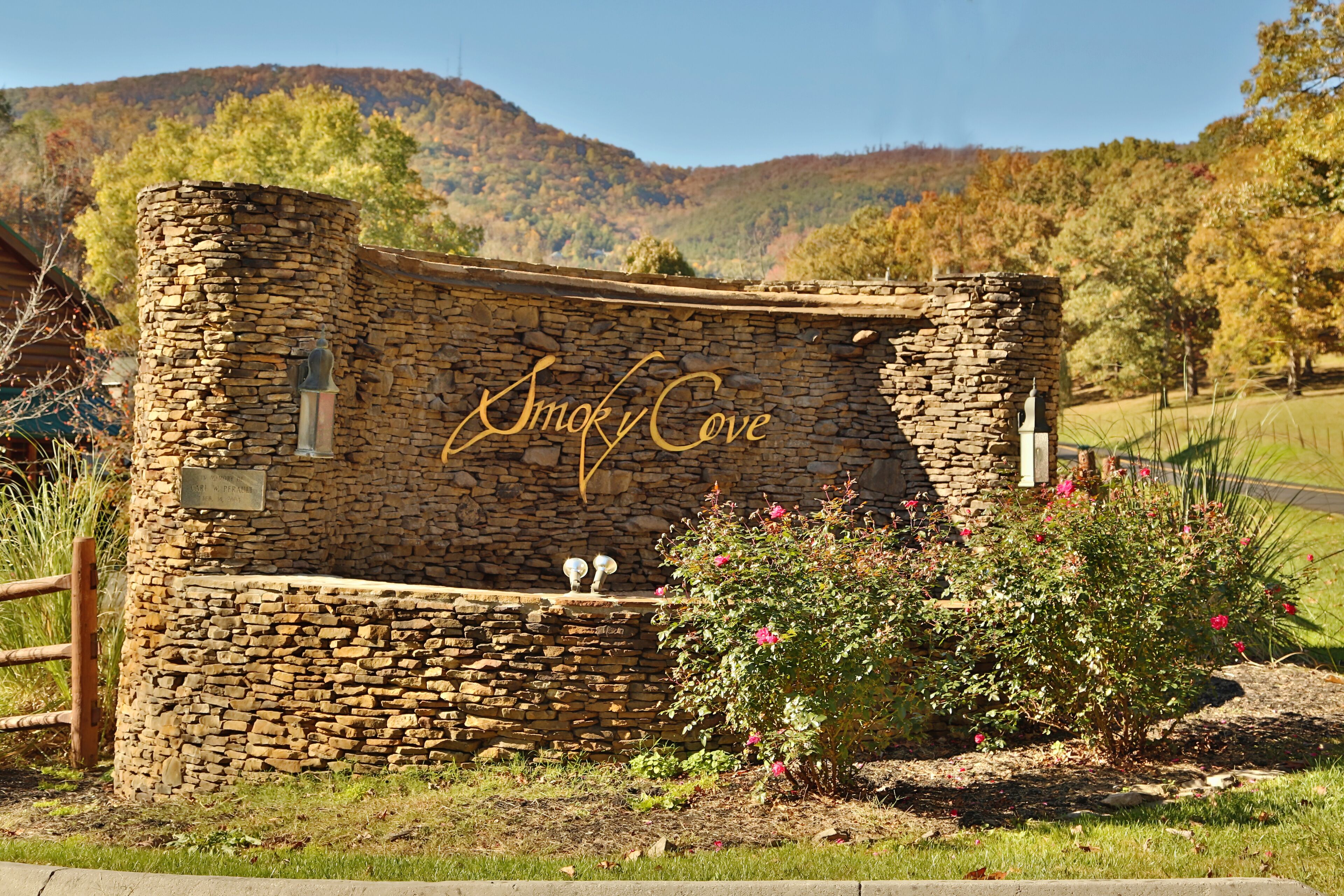 A stone building with the name "Smoky Cove" carved into it, surrounded by a garden with pink flowers and a wooden fence.