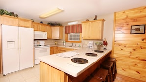 A kitchen with wooden cabinets, a white refrigerator, a microwave, and a stove. There are bar stools along the counter. - Pinnacle View 7C - Three Bedroom Chalet (Pigeon Forge)