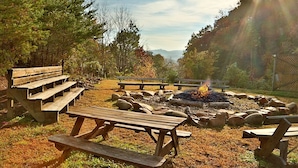 A campsite with picnic tables, a fire pit, and a natural landscape with trees and a distant mountain view. - Pinnacle View 7C - Three Bedroom Chalet (Pigeon Forge)