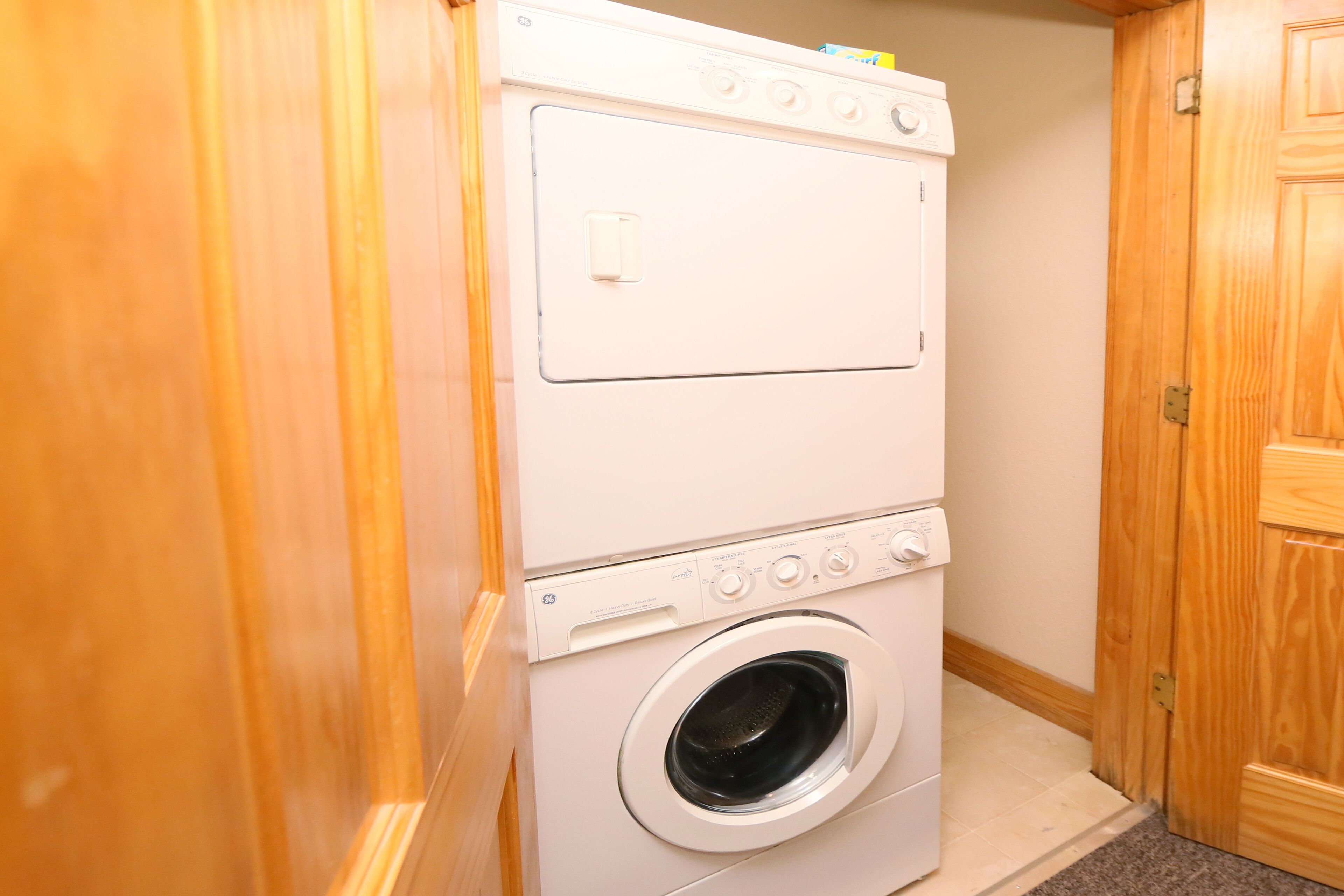 Une buanderie équipée d’un lave-linge et d’un sèche-linge superposés, avec des murs en bois et un sol recouvert de moquette.