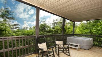 Relax on the deck with a hot tub and two comfortable chairs, surrounded by lush greenery.