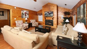 A cozy living room with wooden walls, a fireplace, two sofas, a coffee table, and a ceiling fan. - Wildwood Falls 4 - Two Bedroom Chalet (Pigeon Forge)