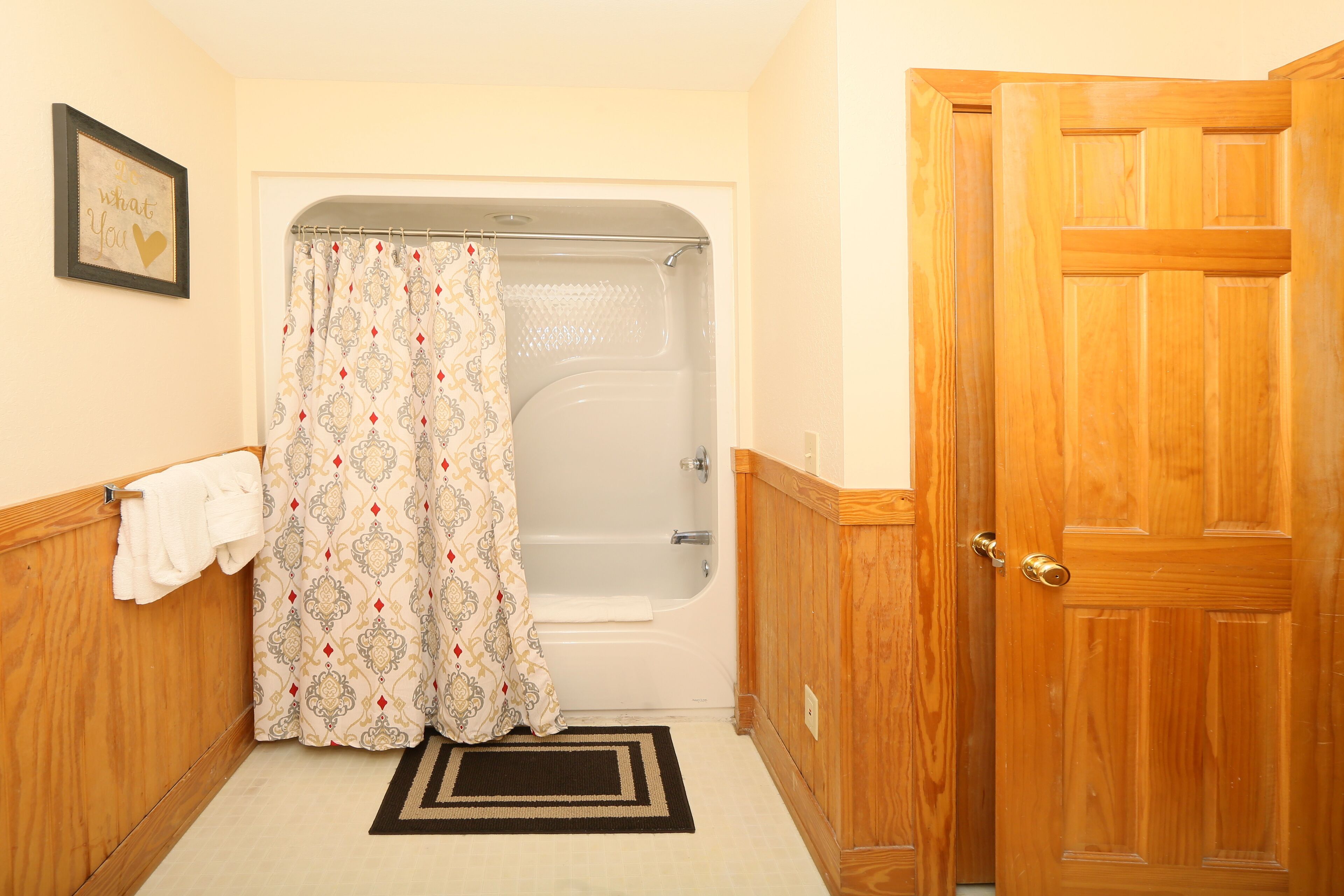 Une salle de bain avec une baignoire, un rideau de douche, une porte en bois et un porte-serviettes.