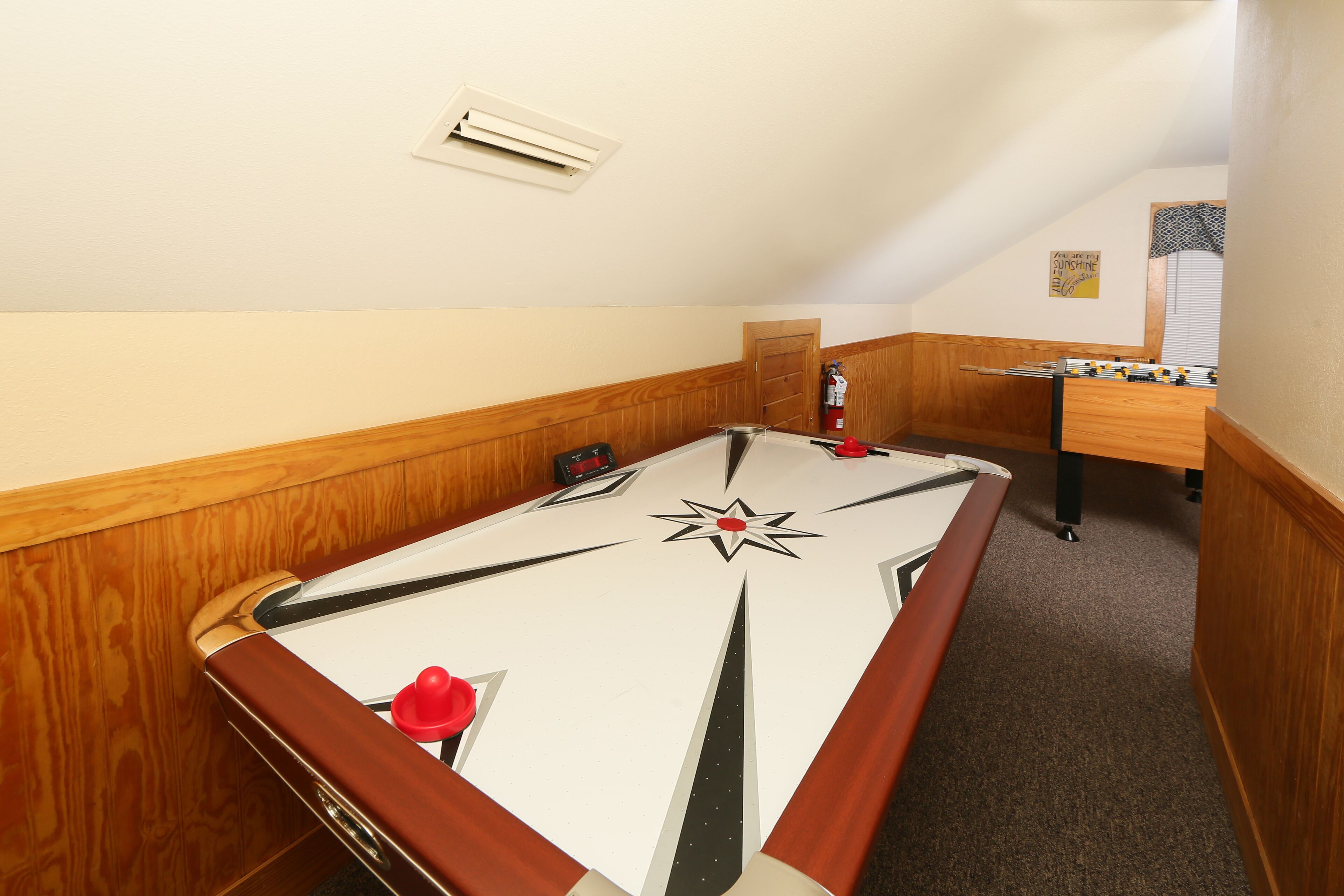 Una mesa de billar en una sala con paneles de madera y un escritorio de madera, con una mesa de fútbol de mesa al fondo.