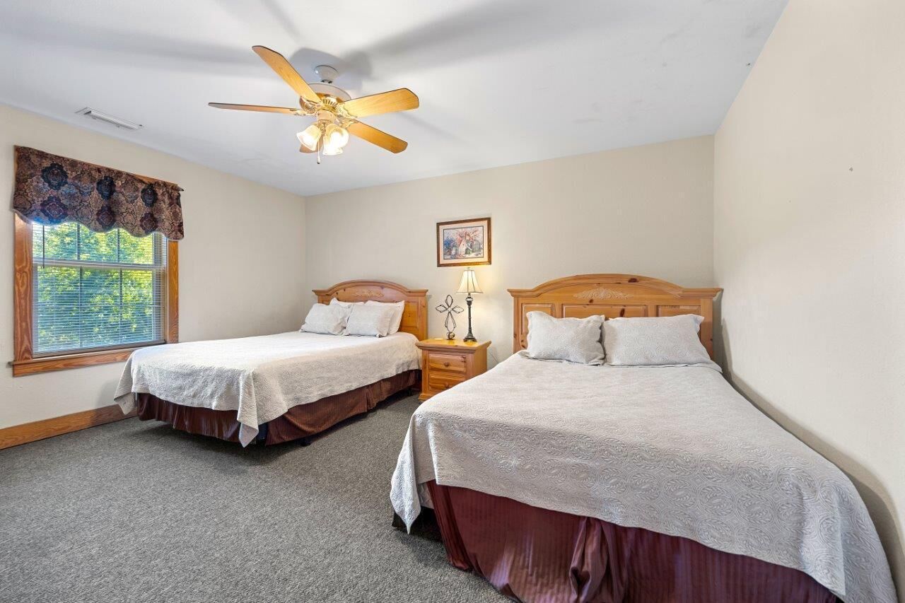 A bedroom with two single beds, a ceiling fan, a window with a decorative valance, and a nightstand with a lamp.