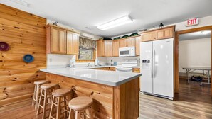 A kitchen with wooden cabinetry, a white refrigerator, and a large island with stools. - Poplar Point Condo Unit 12D - Two Bedroom Condo (Pigeon Forge)