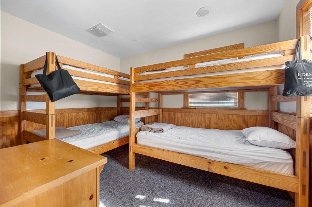 Een slaapkamer met stapelbedden van hout, een bureau en een zwarte tas die aan het bed hangt.
