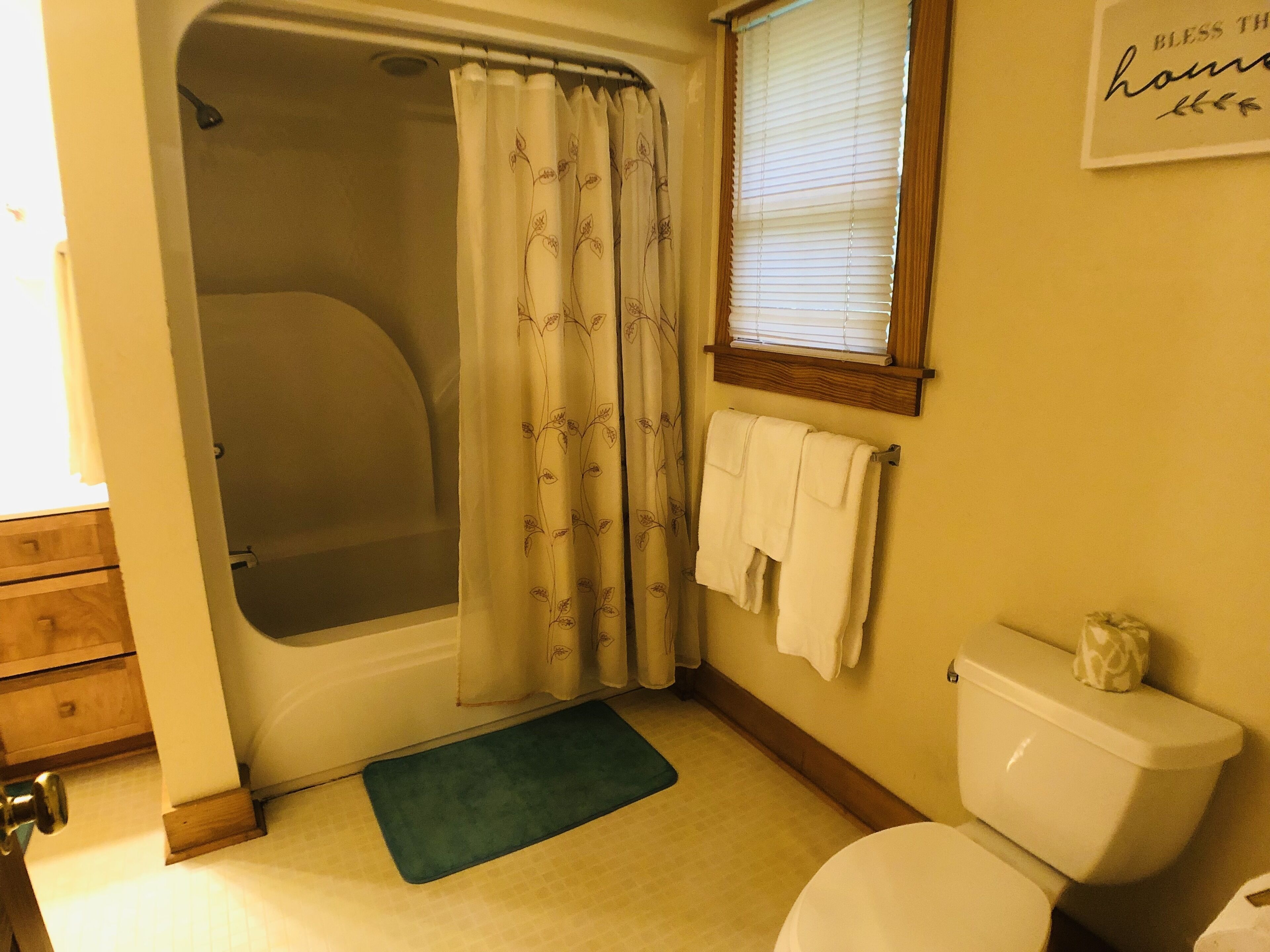 A bathroom with a bathtub, toilet, and a window with blinds.