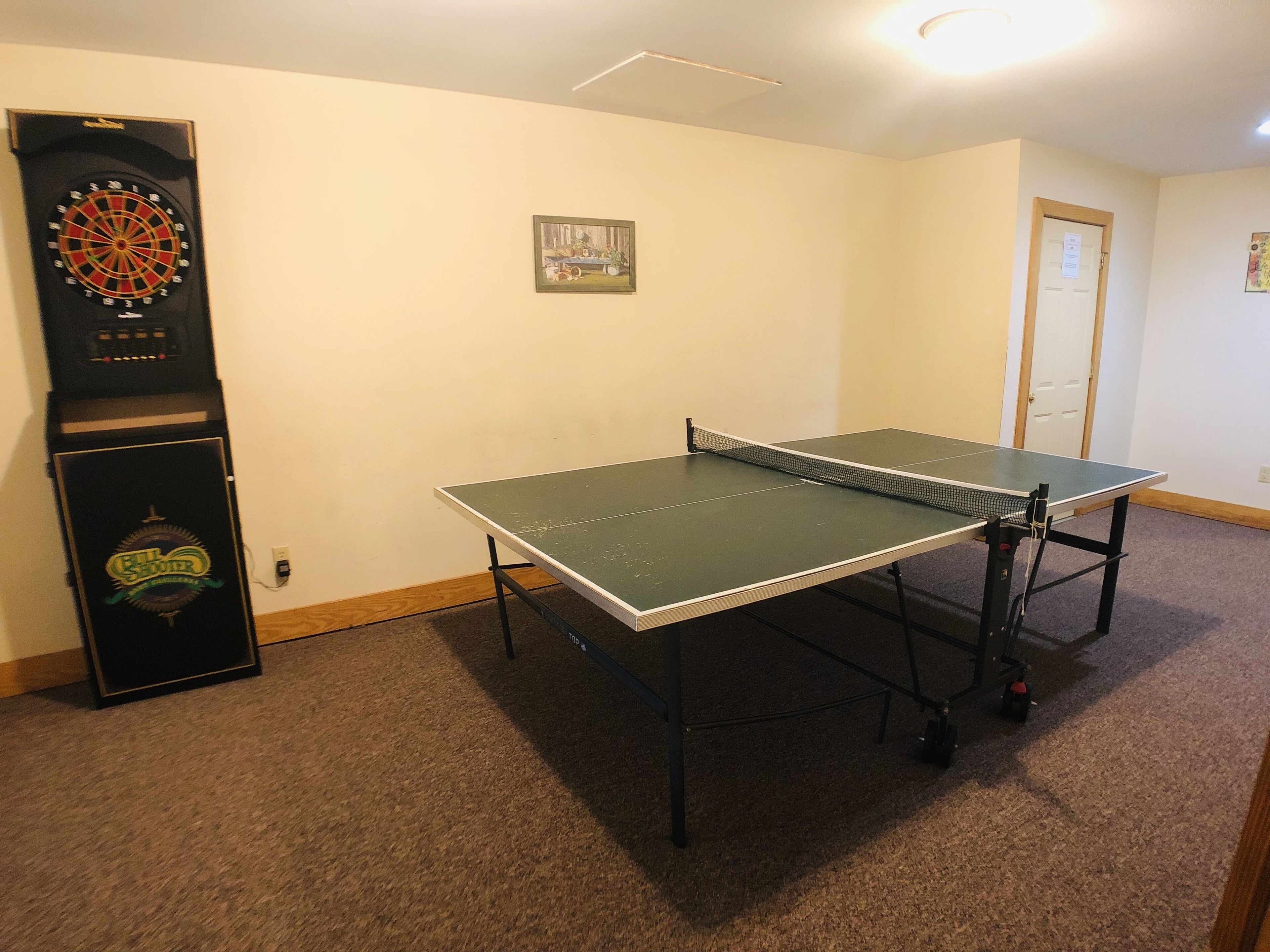 Ein Raum mit Tischtennisplatte, Dartscheibe und einer Tür.