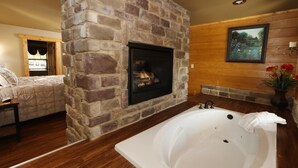 Ein Badezimmer mit Kamin aus Stein, einer großzügigen Badewanne, Holzwänden und einem Gemälde.