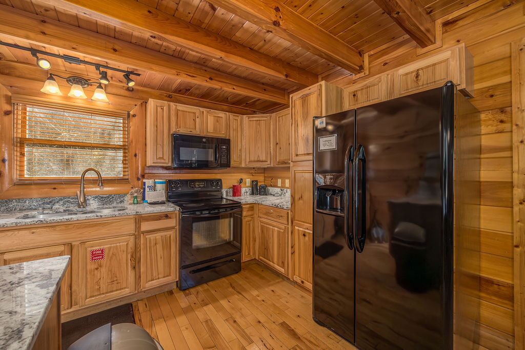 A wooden cabin-style kitchen with a stainless steel refrigerator, a microwave, and a stove.