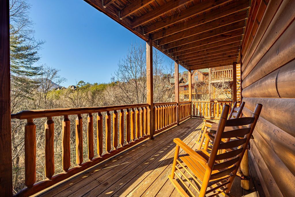 A wooden deck with a railing, wooden chairs, and a view of a mountainous landscape.