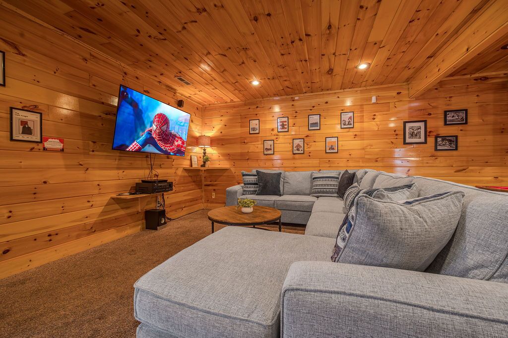 L’intérieur d’un chalet confortable, avec une grande télévision, un canapé gris et des tableaux encadrés accrochés aux murs.