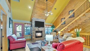 A spacious living room with a fireplace, red leather sofas, a wooden staircase, and a television mounted on the wall. - Splash Mountain Lodge (Gatlinburg)