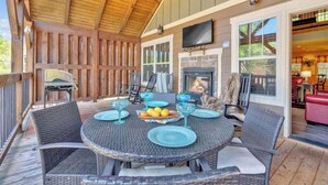 A covered patio with wicker furniture, a stone fireplace, and a television mounted on the wall. - Splash Mountain Lodge (Gatlinburg)