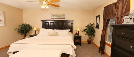 A bedroom with a bed, a bench, a ceiling fan, two nightstands with lamps, a dresser, and a window with curtains.