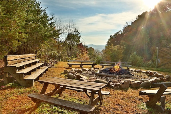 Un camping con mesas de picnic, un pozo de fuego y un paisaje natural con árboles y una vista distante de la montaña.