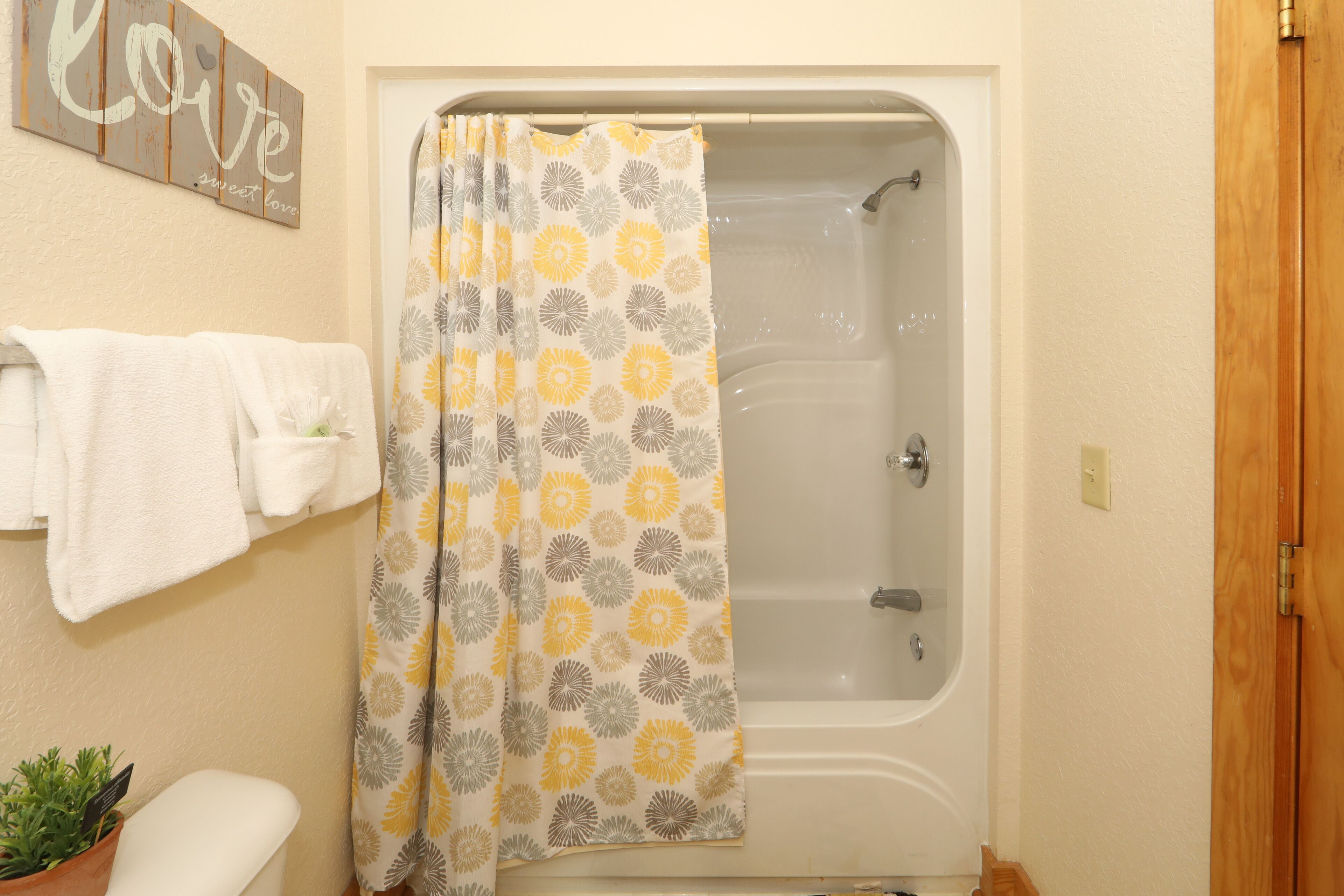 A bathroom with a bathtub, a shower curtain with a floral pattern, a towel rack with white towels, and a wooden door.