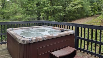 Relax in a hot tub on a raised deck overlooking a serene forest.