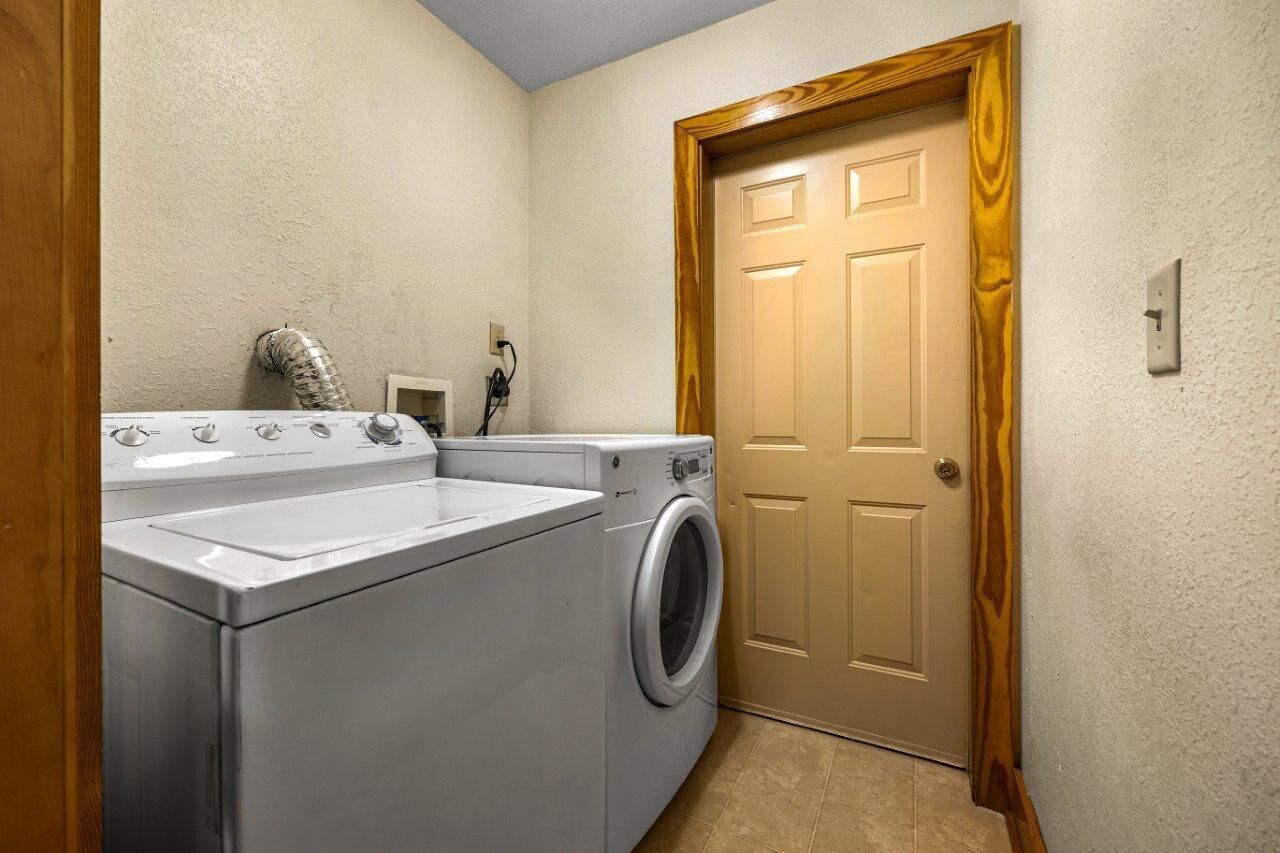 A laundry room with a front-loading washer and dryer, a wooden door, and a light switch on the wall.