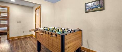 A room with a wooden foosball table, a door, and a painting on the wall.
