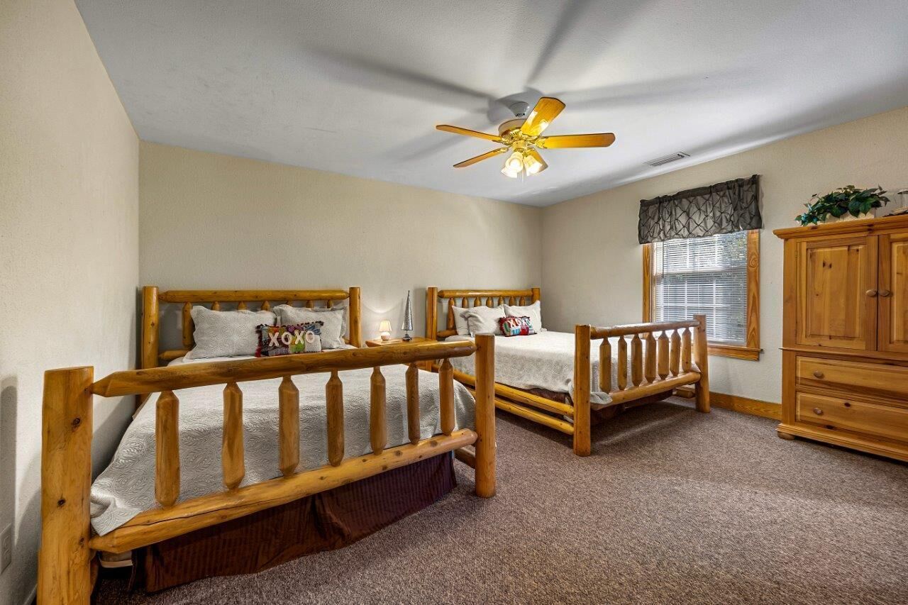 A bedroom with two wooden beds, a ceiling fan, a window with blinds, and a wooden cabinet.