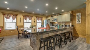 A kitchen with a central island, bar stools, and a dining area with chairs. - Marco Polo - Four Bedroom Chalet (Gatlinburg)