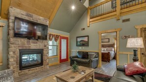 A spacious living room with a stone fireplace, a flat-screen TV, a wooden coffee table, and a leather sofa. - Marco Polo - Four Bedroom Chalet (Gatlinburg)