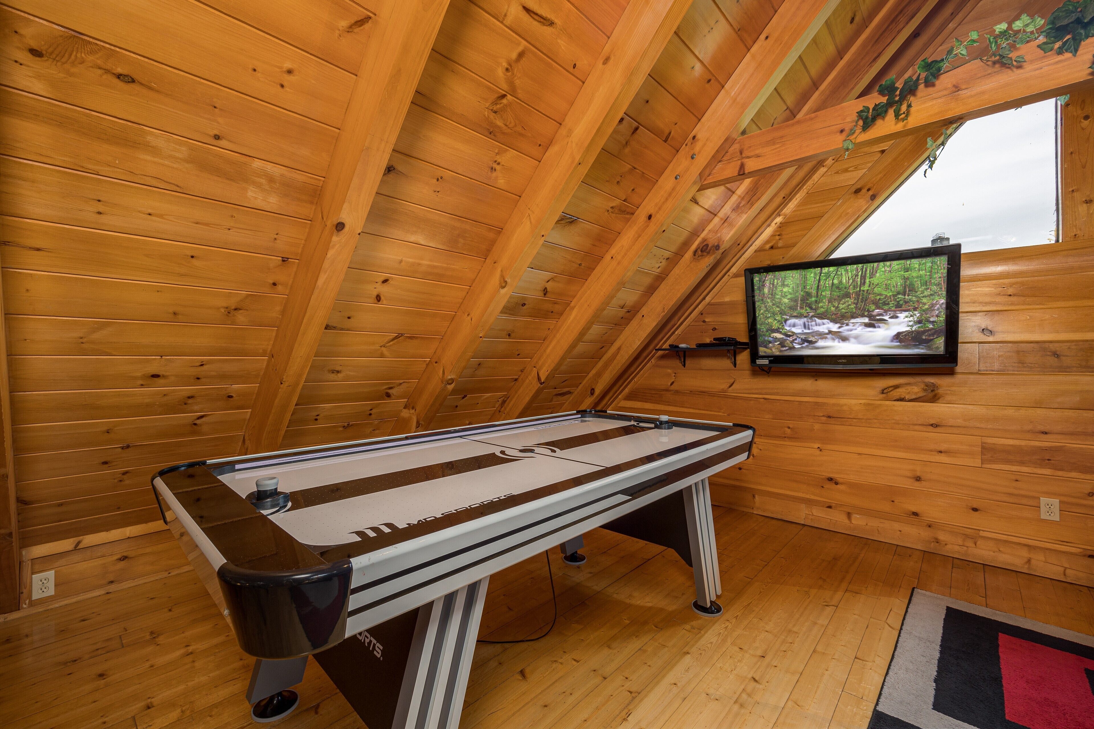 Una mesa de billar en una habitación de madera con un televisor mostrando una escena natural.