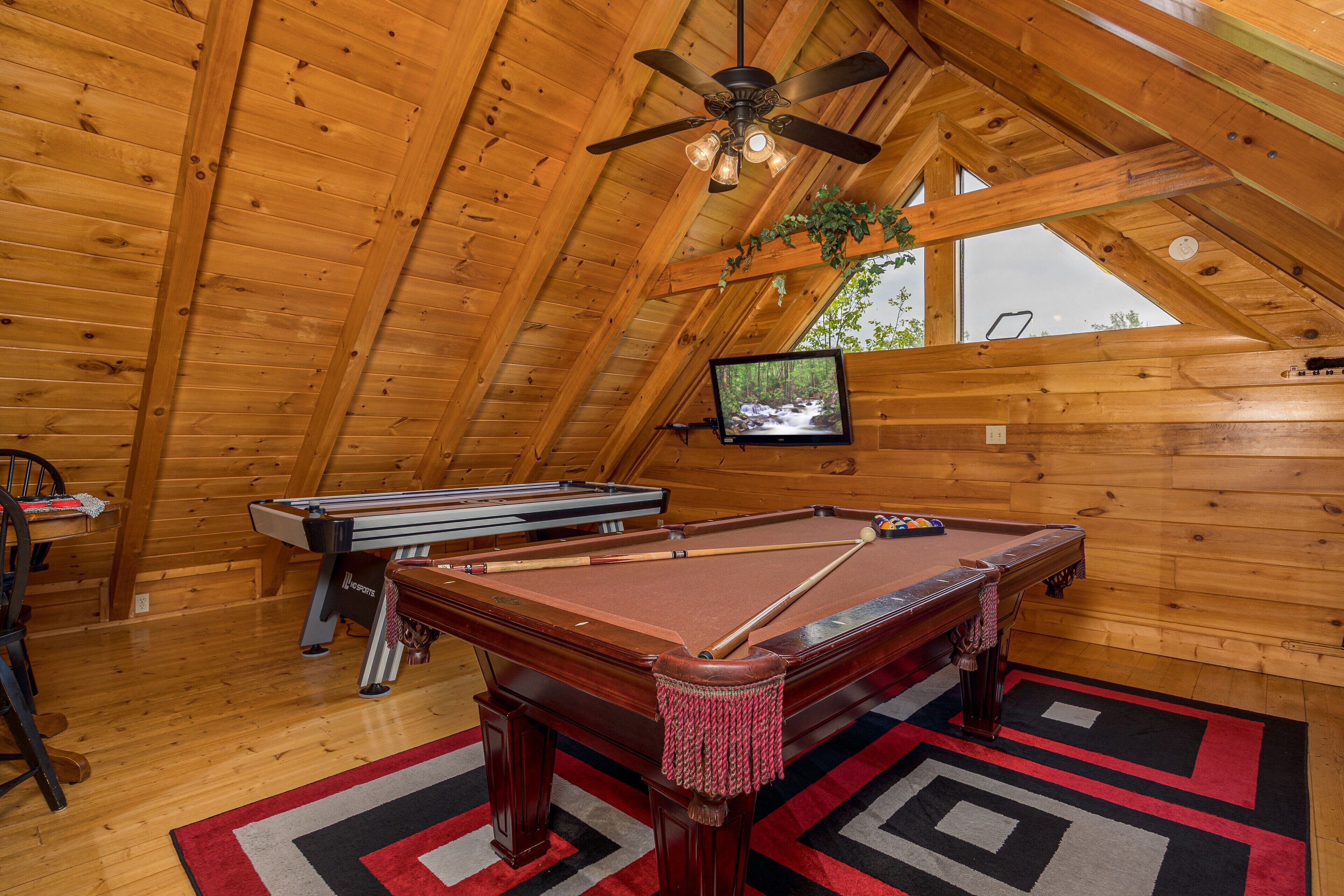 A wooden interior with a pool table, a billiards table, and a ceiling fan.