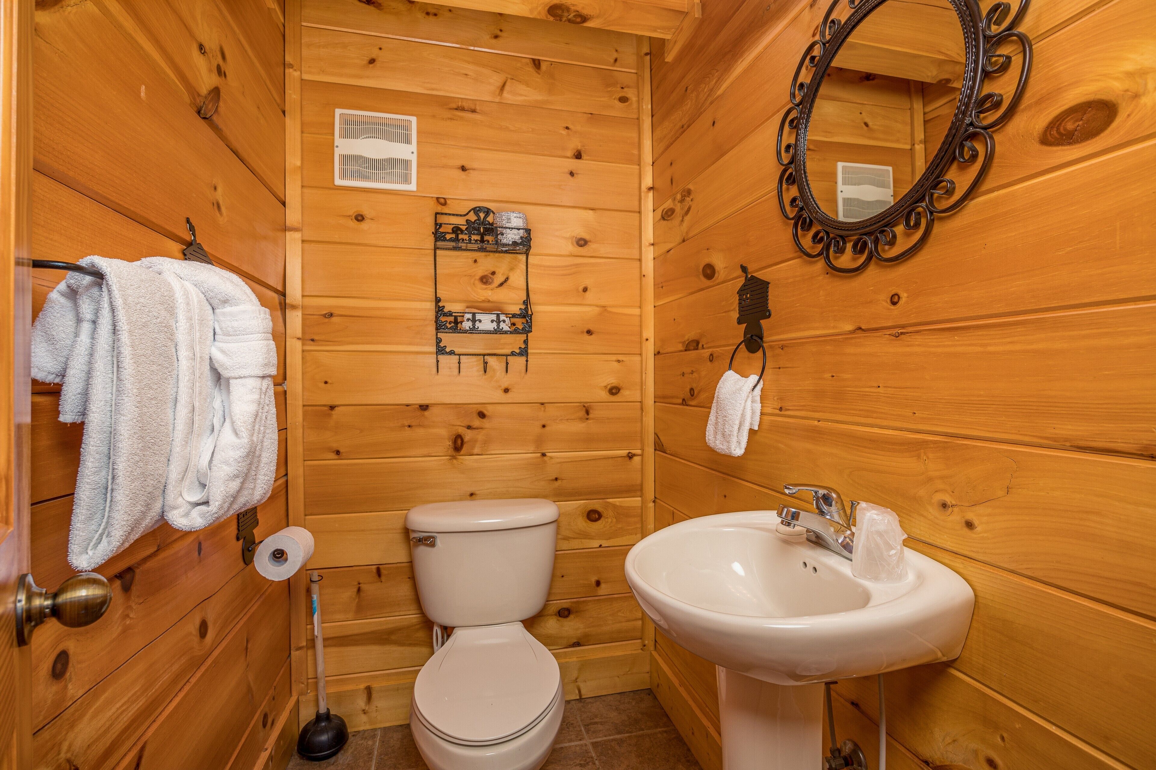 Baño de cabaña de madera con inodoro, lavamanos y espejo.