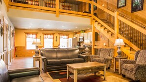 A spacious living room with a leather sofa, patterned armchairs, a wooden coffee table, and a staircase leading to an upper level.