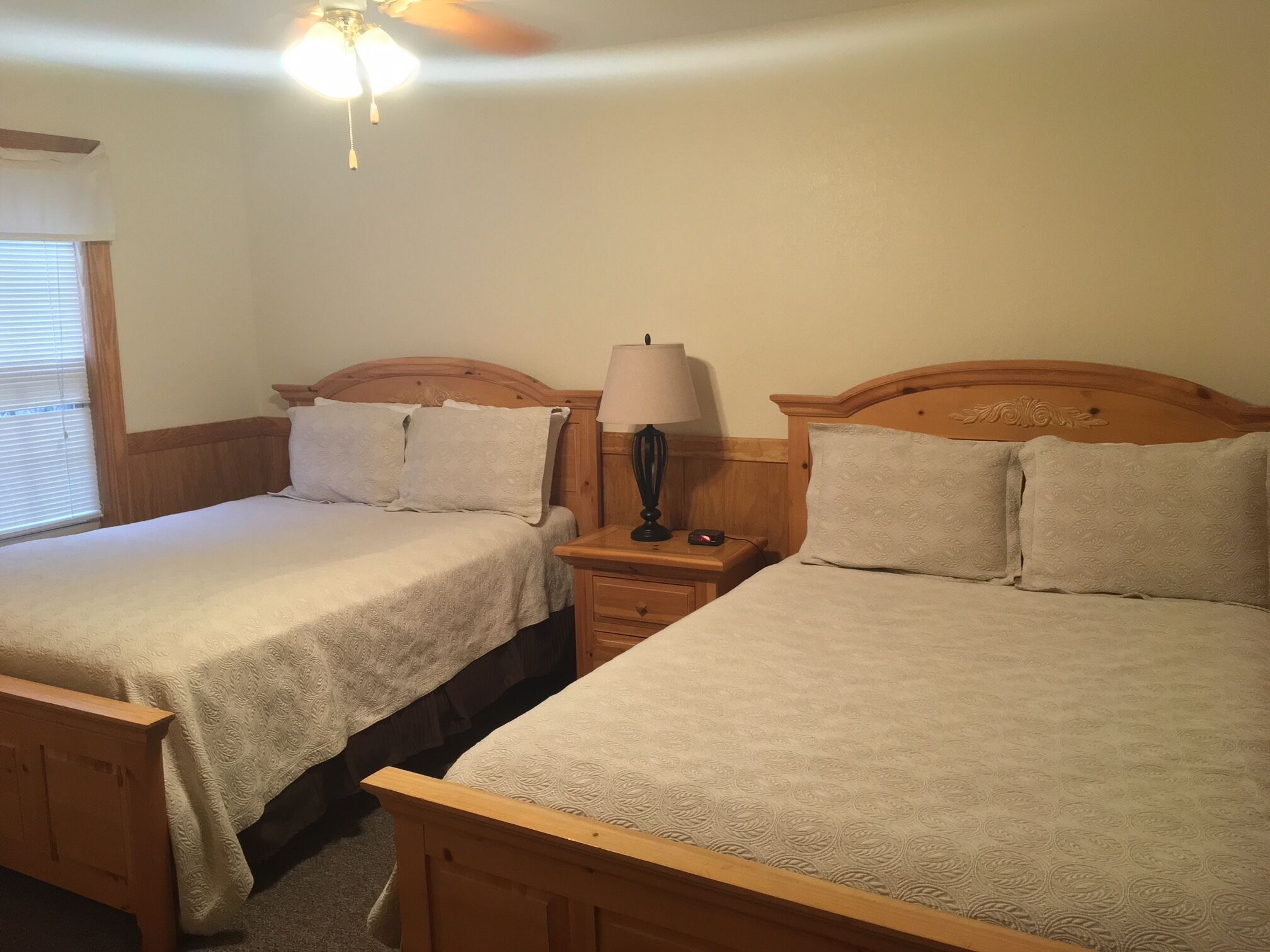 A room with two wooden beds, each with a headboard and a bedside table with a lamp.