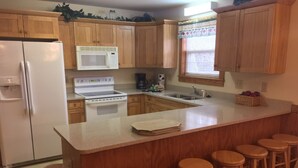 A kitchen with wooden cabinets, a white refrigerator, a stove, a microwave, a sink, and bar stools.