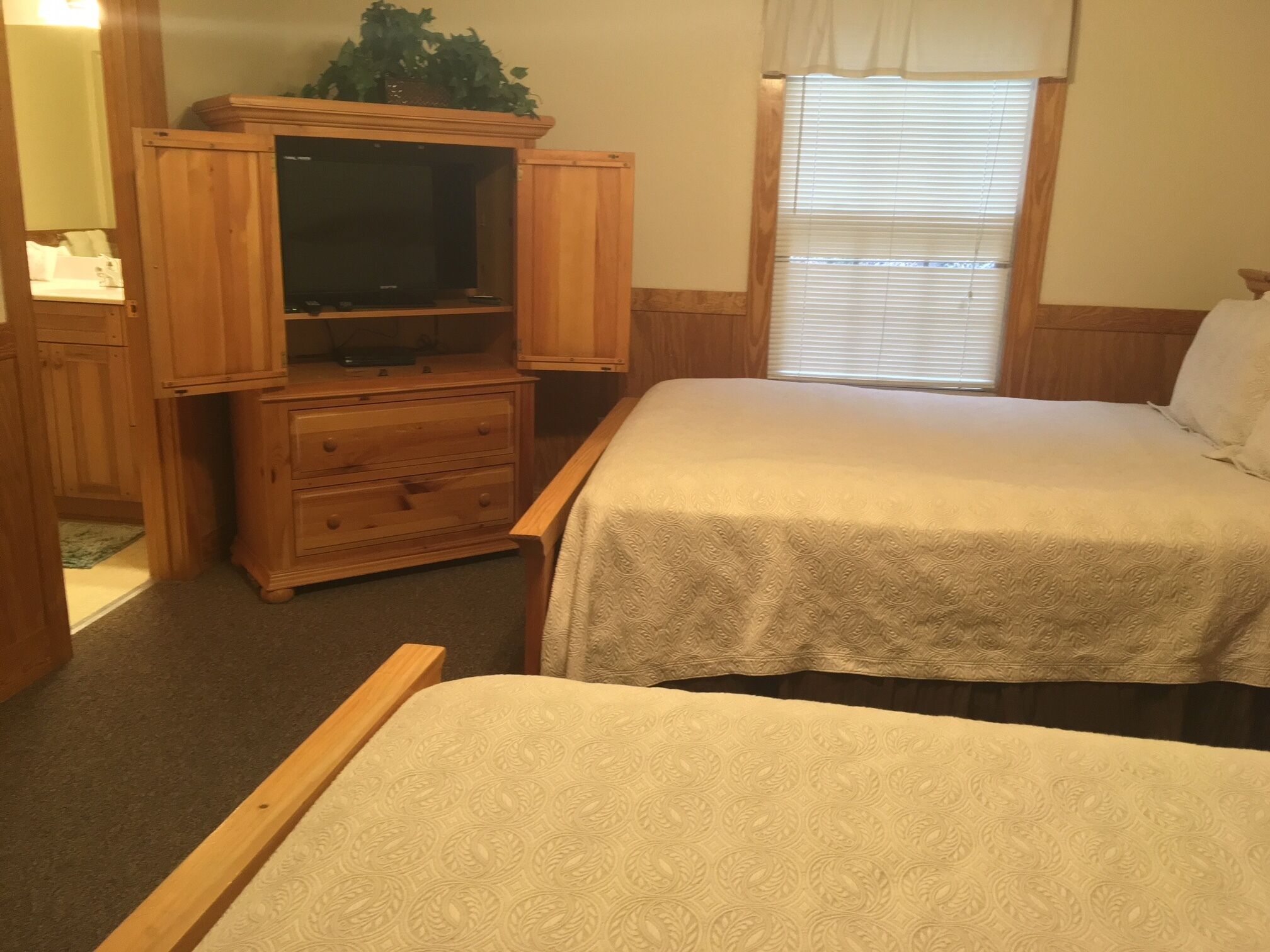 A room with two beds, a wooden cabinet with a television, and a window with blinds.