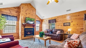 A log cabin interior with a fireplace, wooden walls, a ceiling fan, and a cozy seating area with a coffee table. - Poplar Point Condo Unit 12B - Two Bedroom Condo (Pigeon Forge)