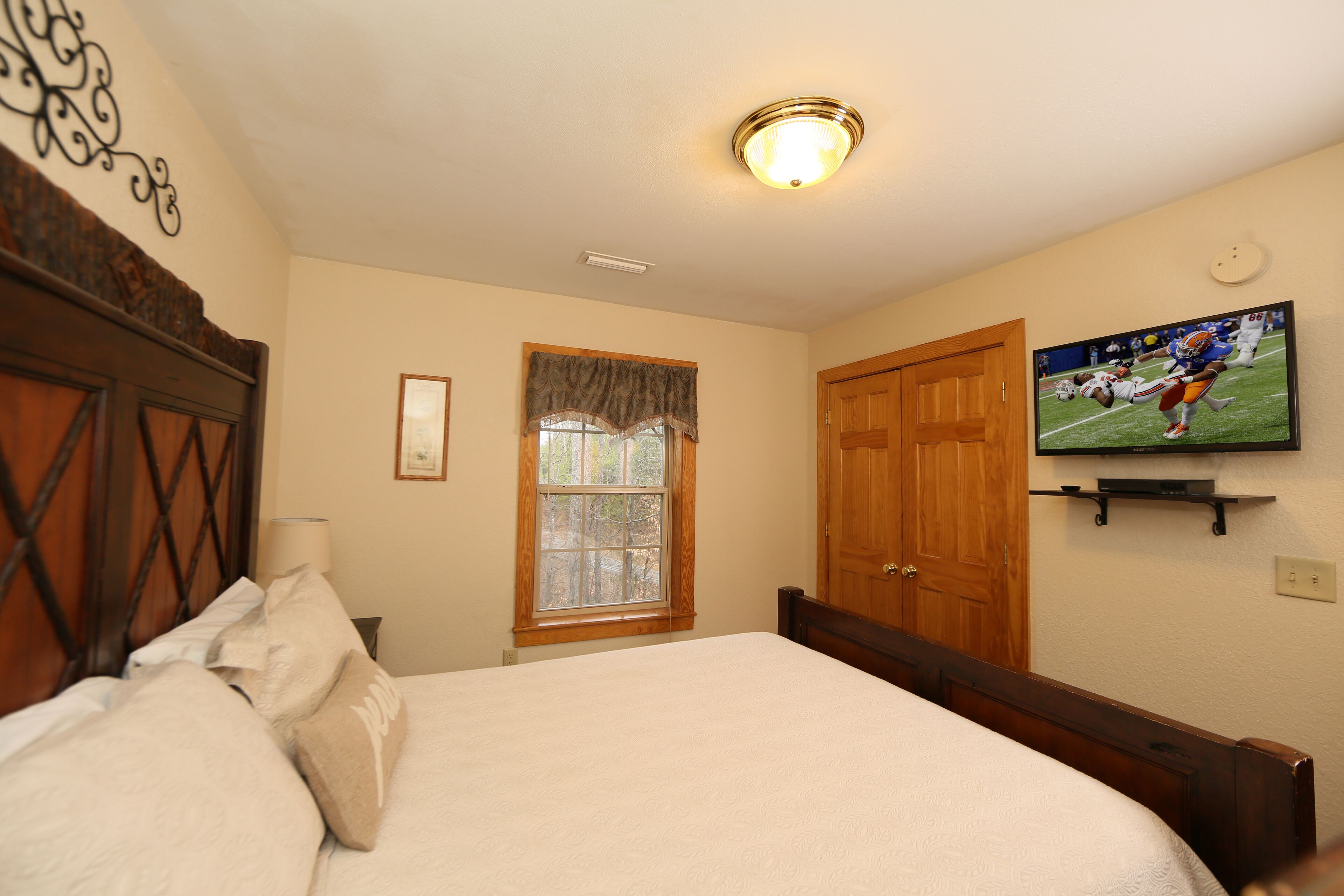 A bedroom with a large bed, a television mounted on the wall, a window with curtains, and a wooden door.