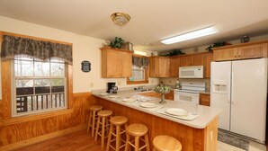 A kitchen with wooden cabinets, a central island with stools, a microwave, a refrigerator, and a window with a view. - Ivy Falls 9 - Five Bedroom Chalet (Pigeon Forge)