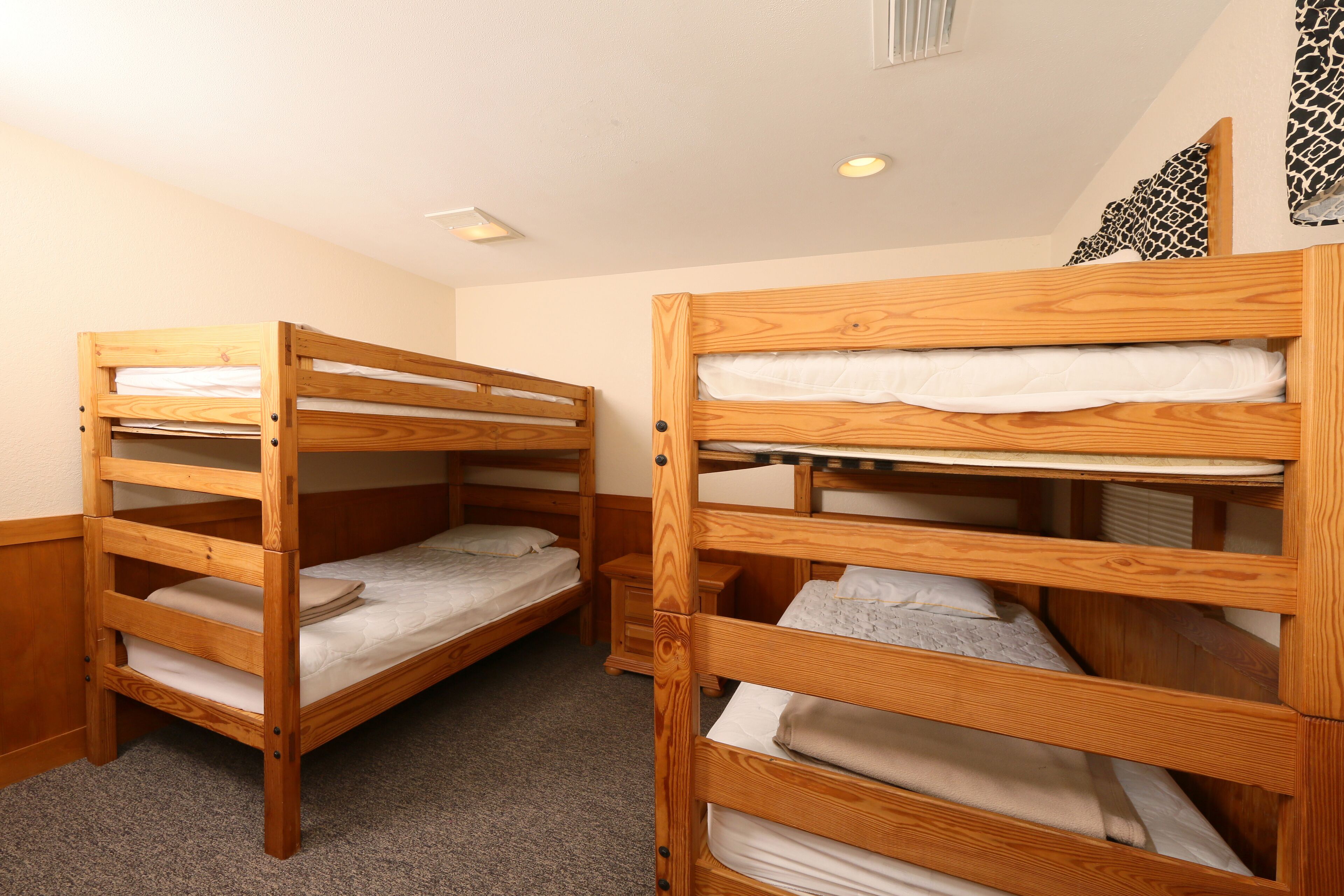 Two bunk beds with wooden frames and white bedding, a small bedside table, and a wall-mounted shelf.