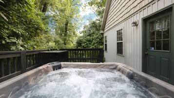 Relax in a serene outdoor hot tub surrounded by lush greenery and a wooden deck.