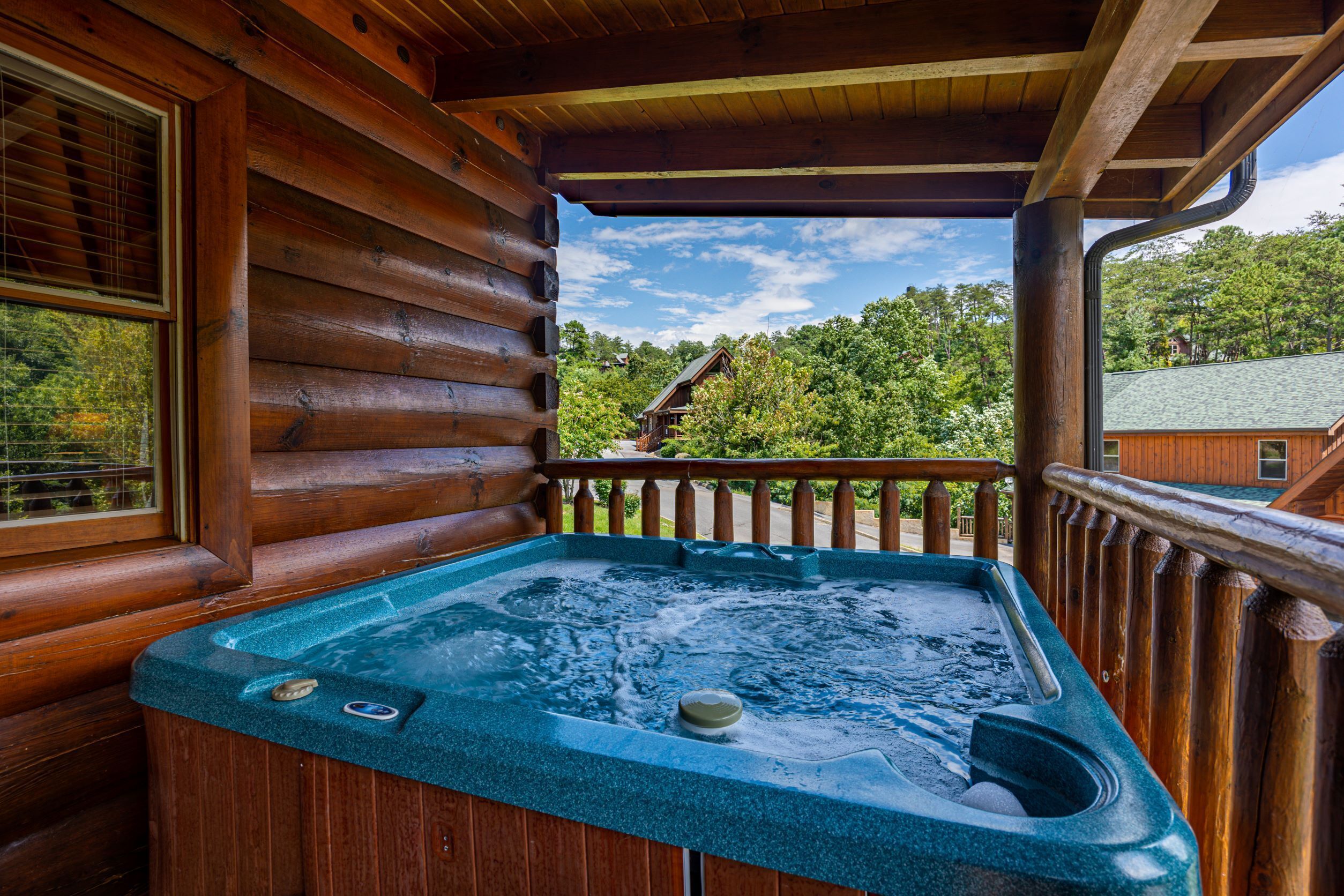 Uma cabana de madeira com banheira de hidromassagem numa varanda, rodeada por árvores.