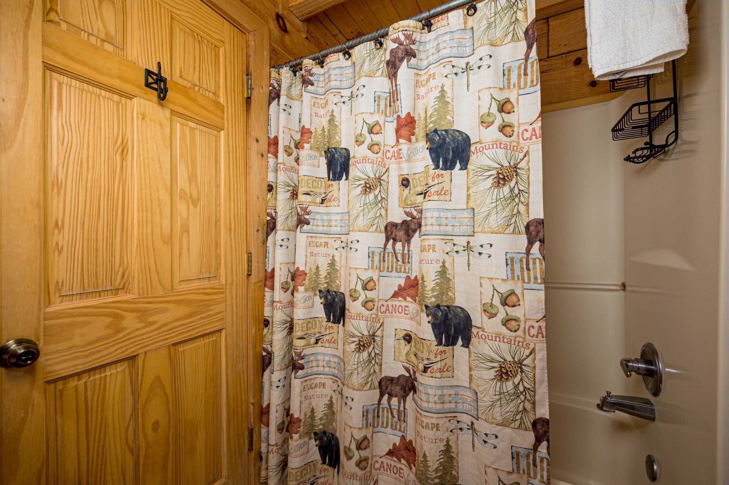 A wooden door with a metal handle, a shower curtain with nature-themed prints, and a white towel hanging on a rack.