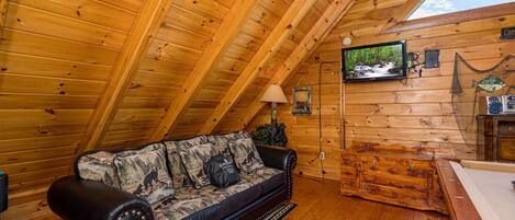 A cozy cabin interior with a wooden ceiling, a leather sofa, a television, and a wooden cabinet.