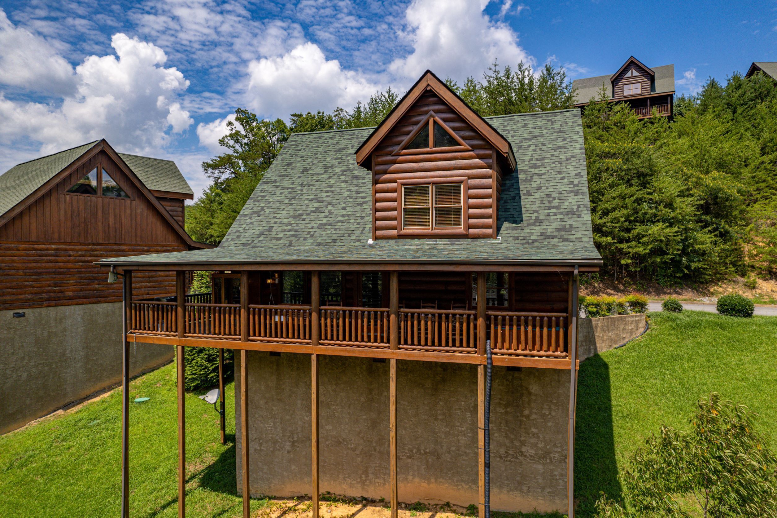 A log cabin with a balcony, surrounded by a grassy yard and trees.