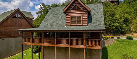 A log cabin with a balcony, surrounded by a grassy yard and trees.