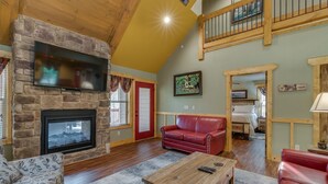 A spacious living room with a stone fireplace, a red leather sofa, and a wooden coffee table. - Swimmin in the Smokies - Six Bedroom Chalet (Gatlinburg)