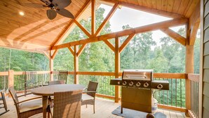 A covered outdoor deck with a wooden table and chairs, a grill, and a view of the forest. - Swimmin in the Smokies - Six Bedroom Chalet (Gatlinburg)