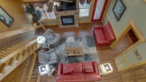 A spacious living area with a red leather sofa, a wooden coffee table, and a fireplace. A staircase with wooden railings leads to an upper level. - Swimmin in the Smokies - Six Bedroom Chalet (Gatlinburg)
